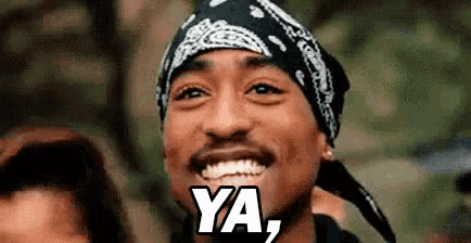 a close up of a man wearing a bandana and smiling with the words `` ya '' written on his face .