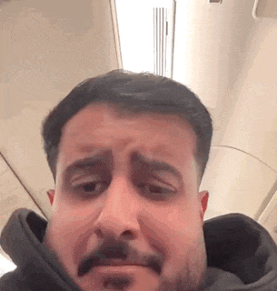 a man with a mustache is making a funny face while sitting on a plane .