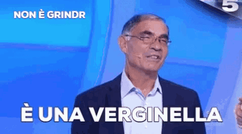 a man in a suit and glasses is standing in front of a blue background with the words e una verginella written on it .