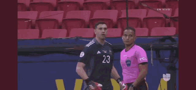 a soccer player wearing a jersey with the number 23 on it is standing next to a referee .