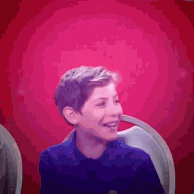 a young boy in a blue shirt is smiling in front of a pink background