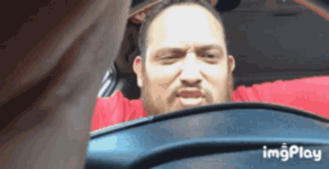 a man with a beard is sitting in a car with a red curtain behind him ..