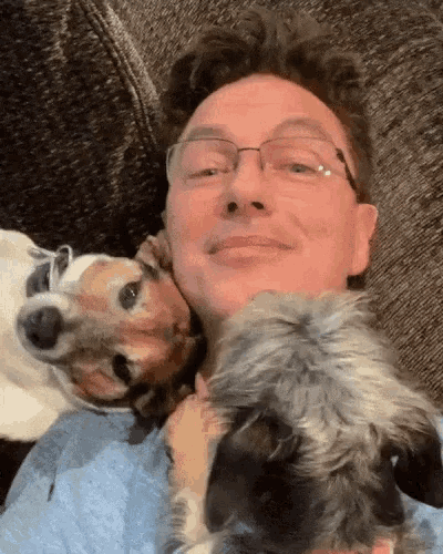 a man wearing glasses is laying on a couch with two dogs