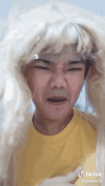 a man wearing a blonde wig and a yellow shirt has a tiktok sticker on his face