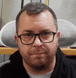 a man with glasses and a beard looks at the camera