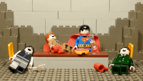 three lego figures are sitting around a table with one of them wearing a superman outfit