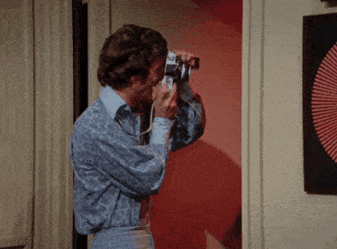 a man in a blue shirt is taking a picture with a camera that says ' nikon ' on the front