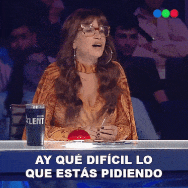 a woman sitting in front of a sign that says ay que dificil lo que estás pidiendo