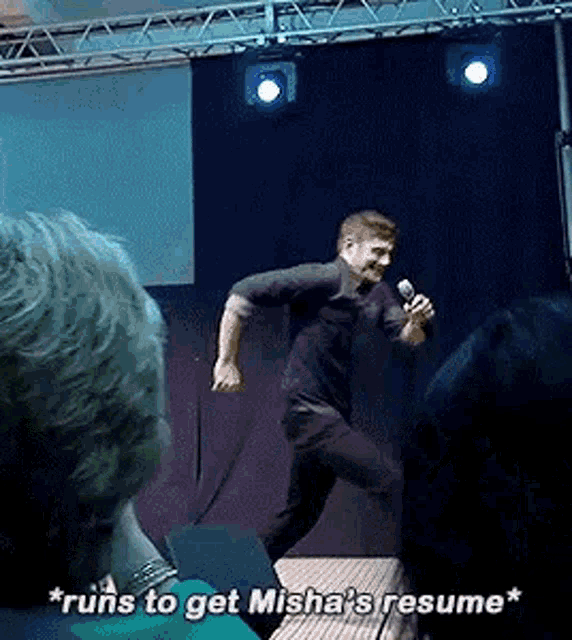 a man is standing on a stage holding a microphone and talking to a crowd .