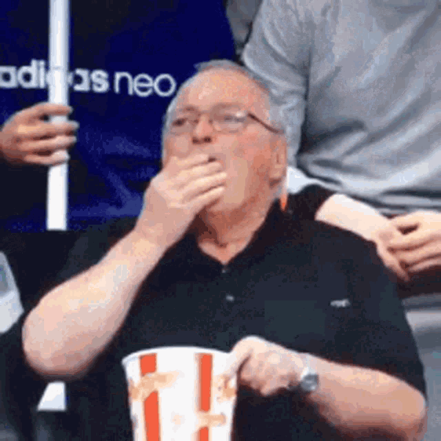 a man is sitting in a stadium eating popcorn and covering his mouth with his hand .