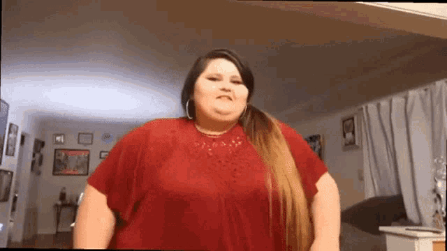 a woman is standing in a living room wearing a red shirt .