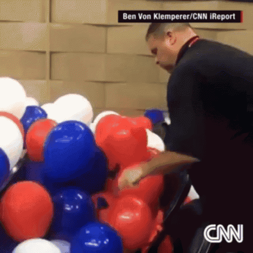 a man is standing in front of a bunch of red white and blue balloons with a cnn logo in the corner
