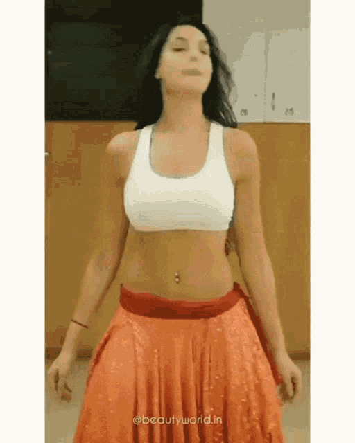 a woman in a white crop top and orange skirt is dancing .