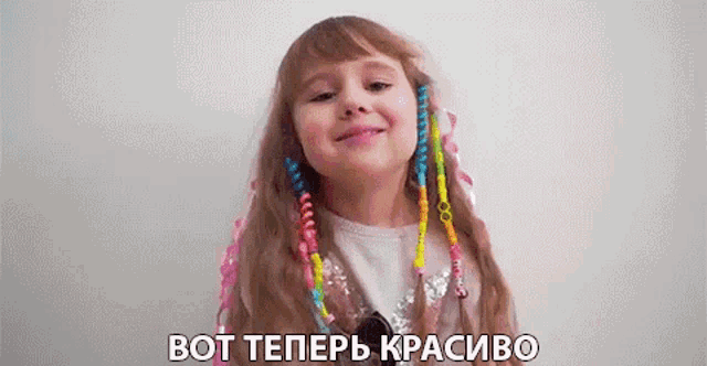 a little girl with colorful beads in her hair is smiling and talking in a foreign language .