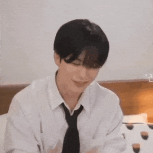 a man in a white shirt and tie is sitting on a bed eating a cupcake .
