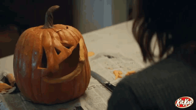 a woman is carving a pumpkin in front of a kitkat sign