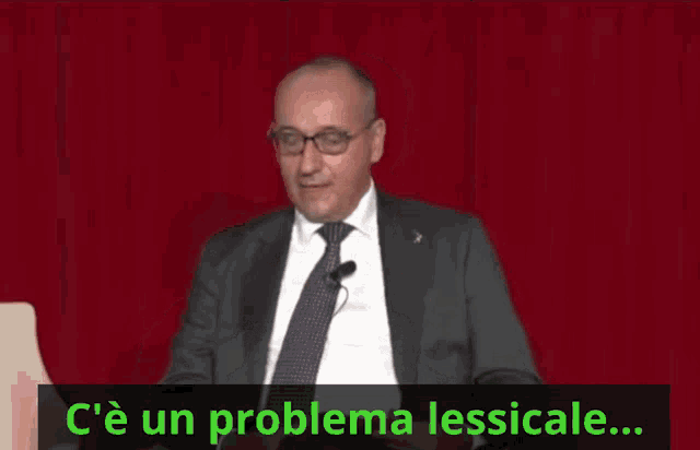 a man in a suit and tie is sitting in front of a red curtain with the words c'e un problema lessicale