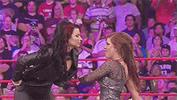 two women are fighting in a wrestling ring while a crowd watches .