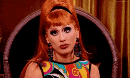 a woman with red hair is sitting in a chair wearing a colorful dress .