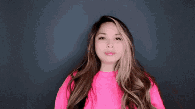 a woman wearing a bright pink sweater is making a funny face