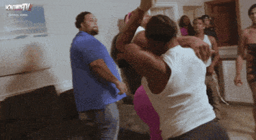 a group of people are dancing in a living room with a tv advertisement behind them