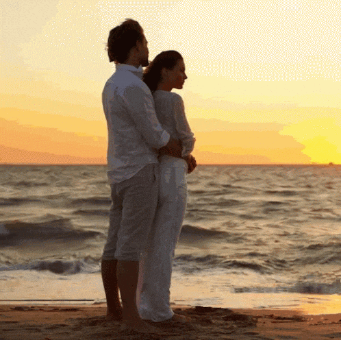 a man and woman standing on a beach looking at the ocean