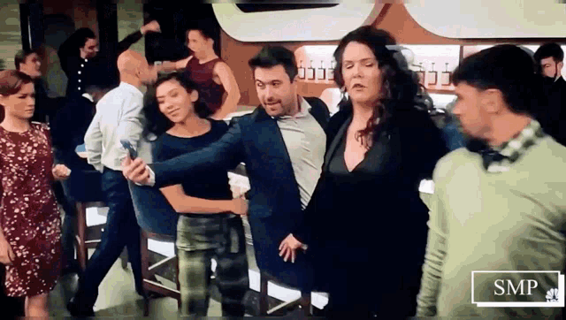 a group of people are dancing in a bar and a man is taking a selfie with his phone .