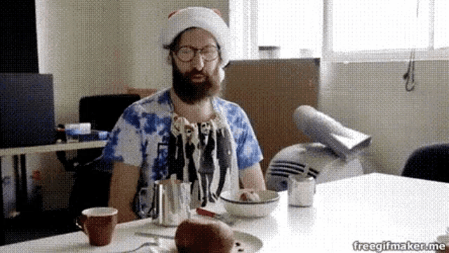 a man with a beard wearing a santa hat is sitting at a table with a bowl of food .