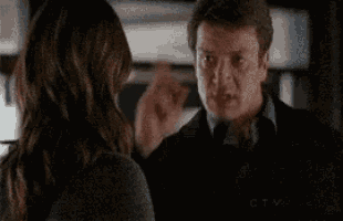 a man and a woman are talking to each other in a room . the man is pointing at the woman .