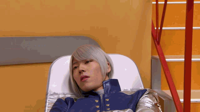 a man in a blue jacket and silver gloves is laying in a hospital bed .
