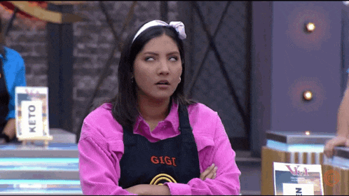 a woman wearing a pink shirt and a black apron with the name gigi on it .