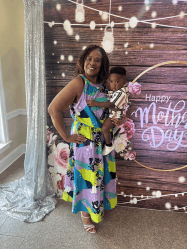 a woman holding a child in front of a happy mothers day sign