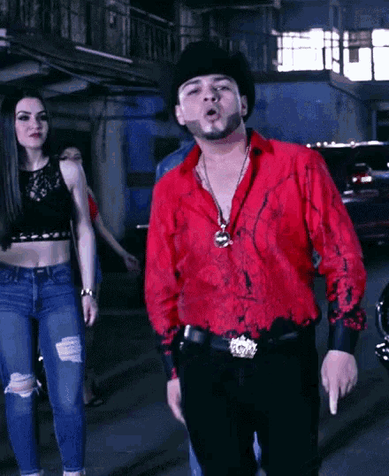 a man in a red shirt and cowboy hat stands next to a woman in a black top