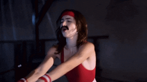 a woman in a red tank top with a mustache and headband is dancing
