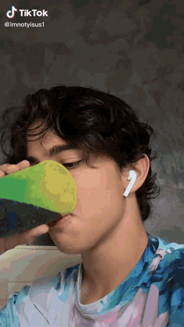 a young man drinking from a green cup with a tiktok watermark on it
