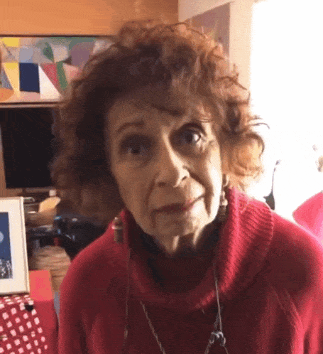 an older woman wearing a red sweater and earrings is looking at the camera