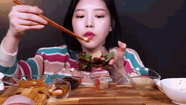 a woman is eating a salad with chopsticks while sitting at a table with bowls of food .