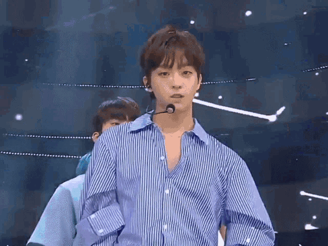 a young man in a blue striped shirt is standing in front of a microphone ..