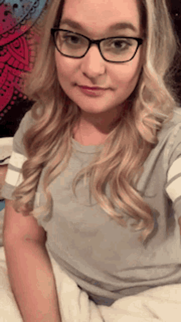 a woman wearing glasses is taking a selfie in bed