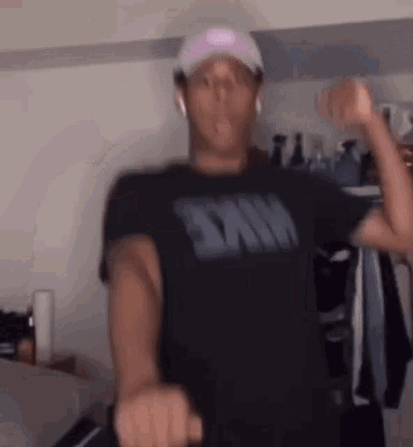 a man wearing a black nike shirt and a pink hat is dancing in a room .