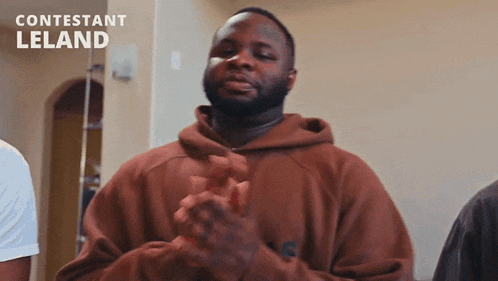a man in a brown hoodie is clapping his hands in front of a wall .