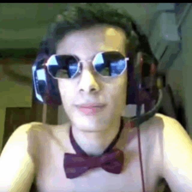 a shirtless man wearing headphones , sunglasses and a bow tie is looking at the camera .