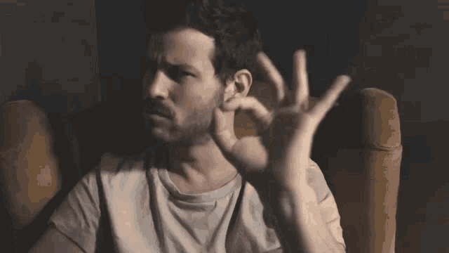 a man with a beard is sitting in a chair and making an ok sign with his hands .