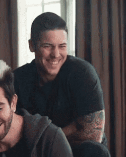 two men are sitting next to each other in a room and smiling .