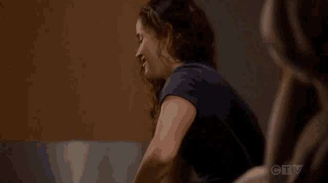 a woman in a blue shirt is sitting next to another woman in a dark room .