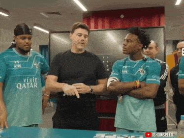 a man wearing a qatar shirt talks to a group of men
