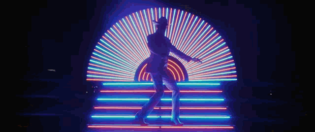 a man in a cowboy hat is dancing in front of a neon light display .