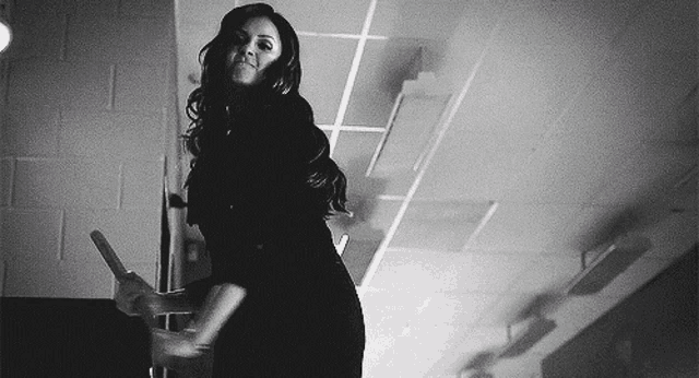 a black and white photo of a woman standing in a room holding a hammer .