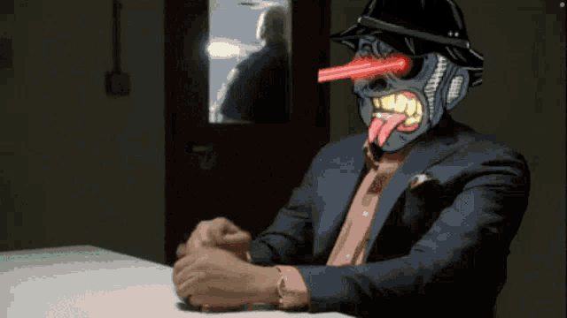 a man in a suit and hat with a tongue sticking out is sitting at a desk