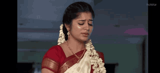 a woman in a red top and white saree is crying while wearing a garland around her neck .